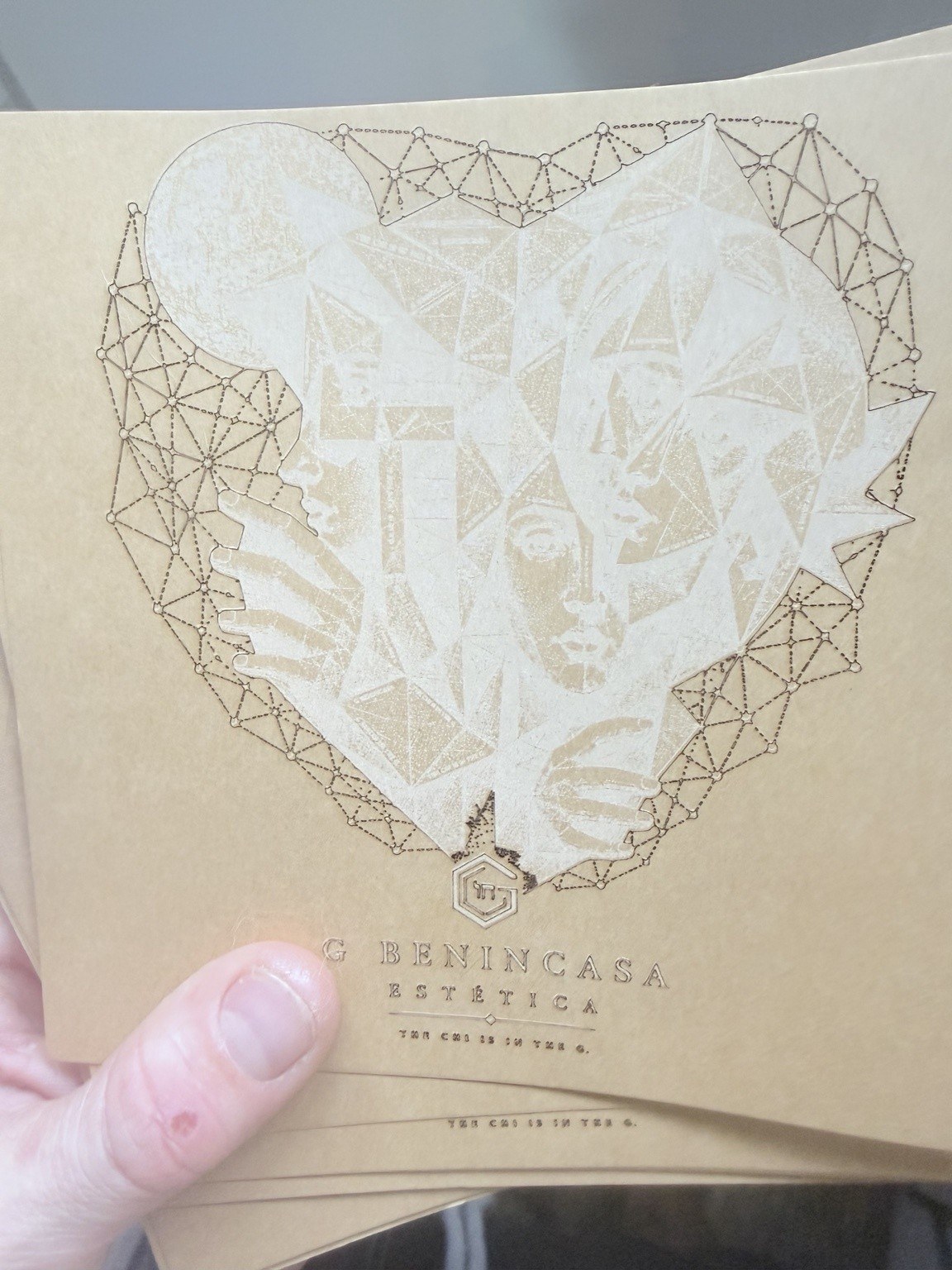 A held cardstock sheet with faceted faces, heart-shaped geometry and the G Benincasa mark.